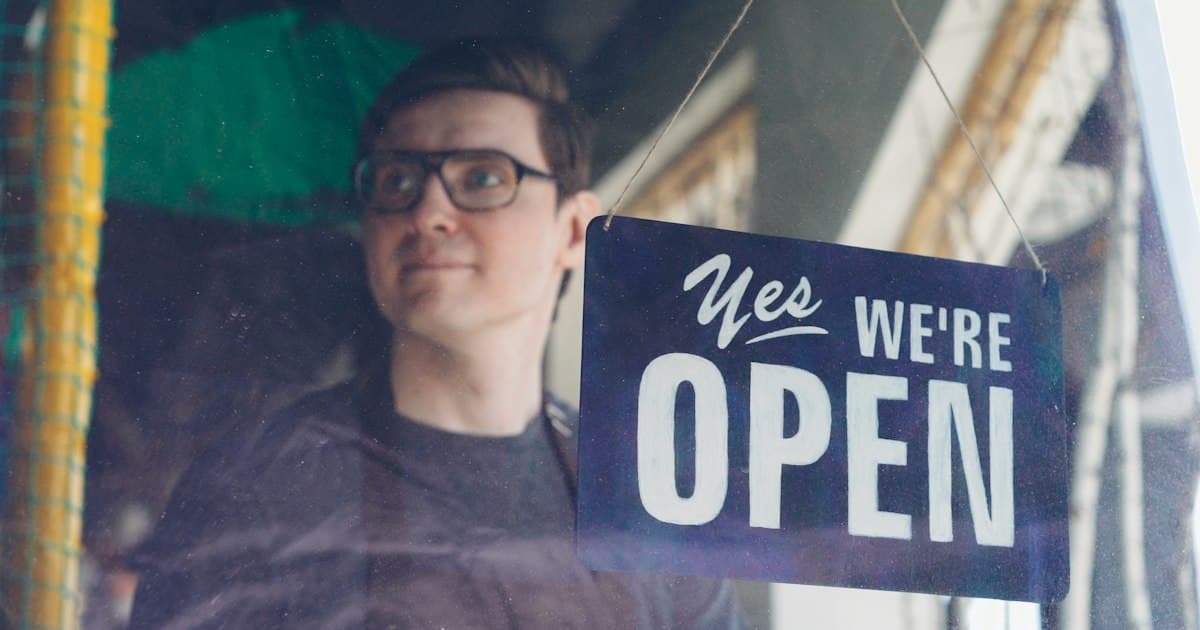 A man proudly displays an "open" sign